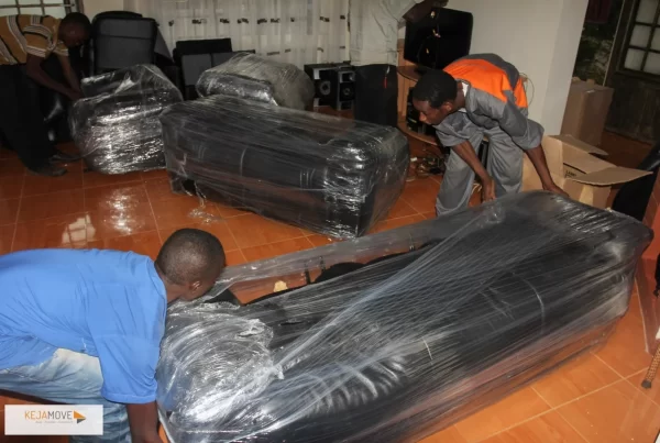 KejaMove movers wrapping sofas in plastic film inside a living room before a move.