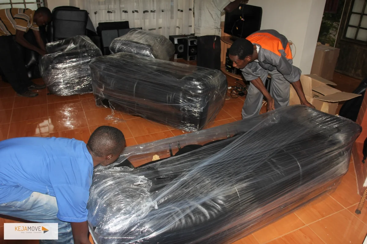 KejaMove movers wrapping sofas in plastic film inside a living room before a move.