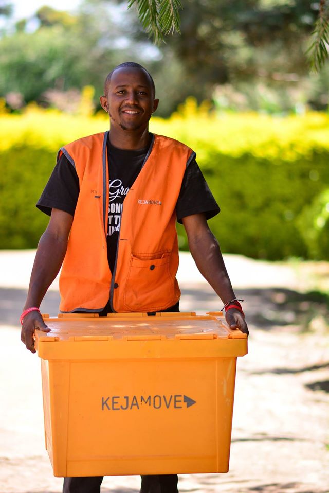 KejaMove mover in an orange branded vest smiling while carrying a KejaMove crate outdoors.